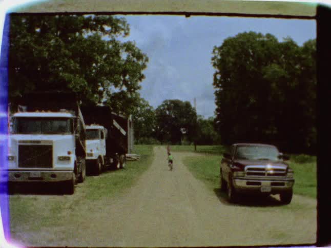A old film of kids riding bikes on a dirt road or driveway
