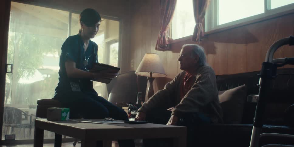 A nurse takes notes on her clipboard while talking with a man at home