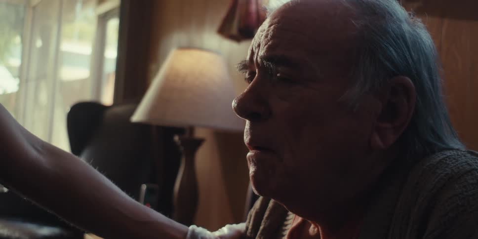 An elderly man is talking to someone while sitting down
