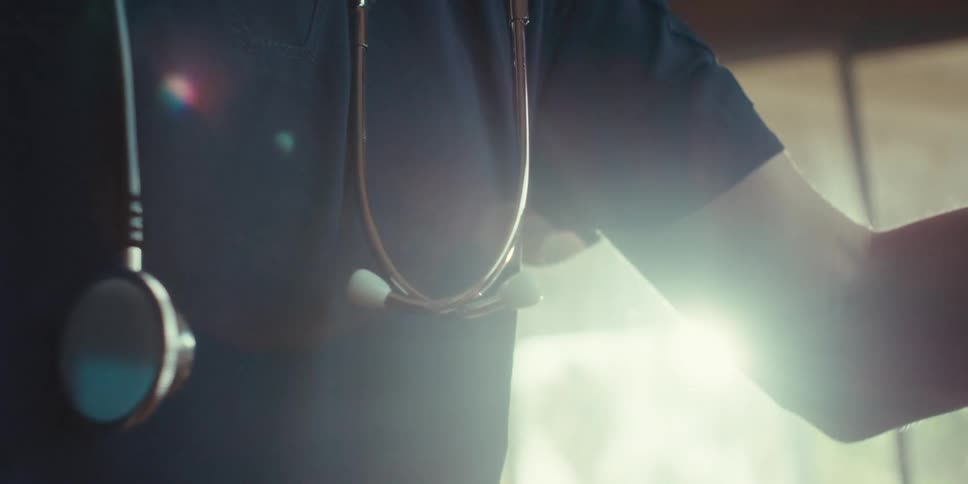 Sunlight streams through the room as a nurse with a stethoscope around her neck attends to a patient at home