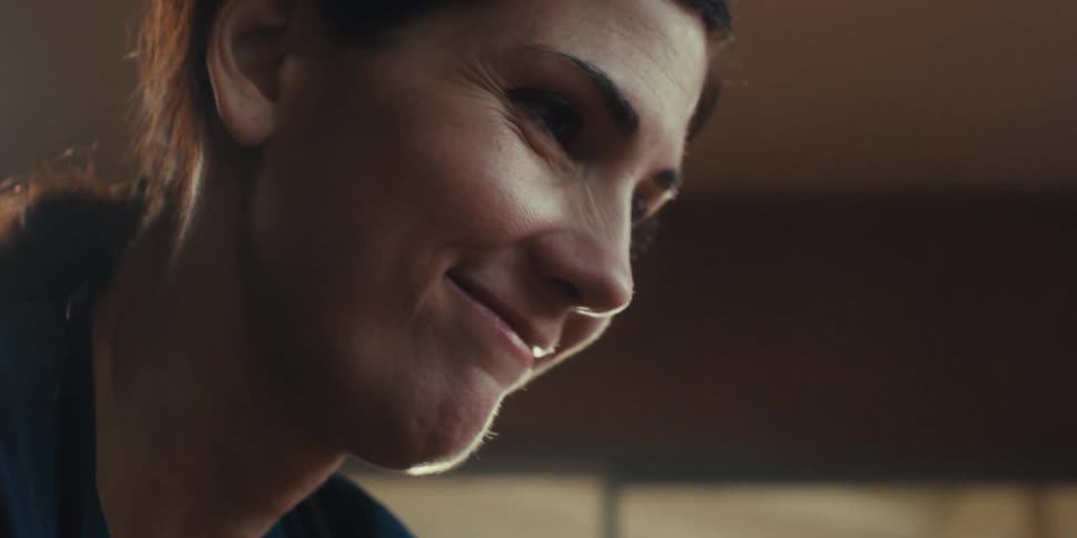 A woman is smiling while standing in a room next to window