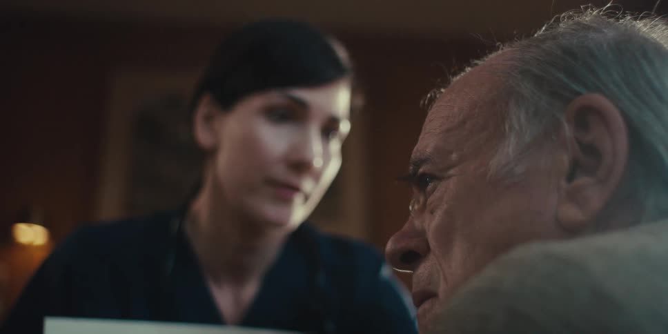 Medical professional smiles while talking to an elderly man during a home visit