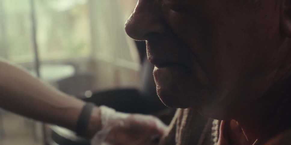 An elderly man holds back tears as a person consoles him by rubbing his shoulder