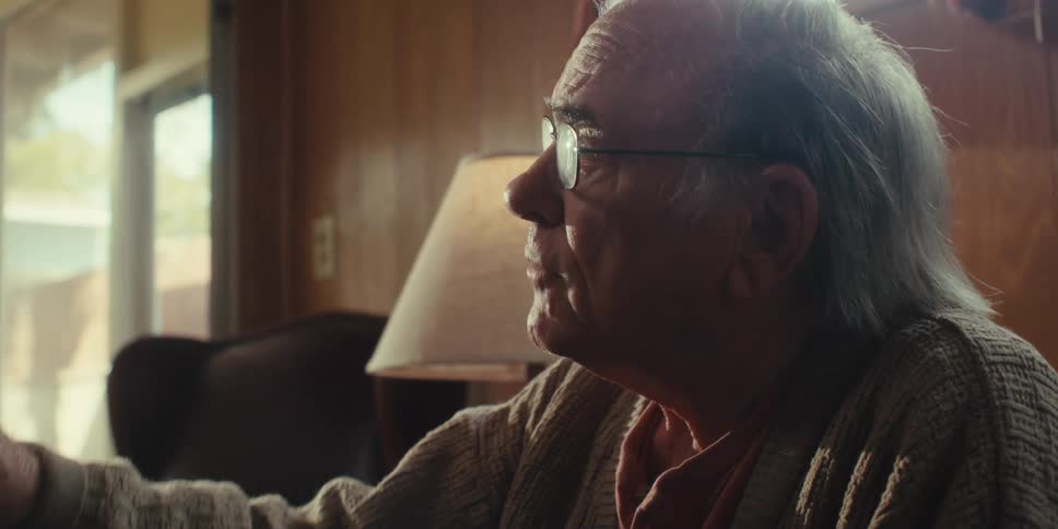 Elderly man listens and talks while sitting in his living room during the daytime