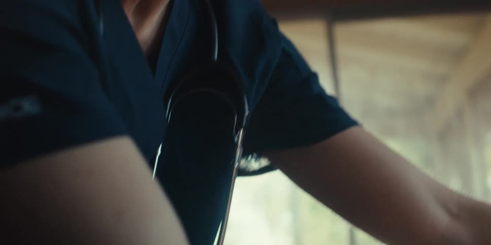 A closeup of a female doctor with a stethoscope around her neck tending to a patient at home bathed in bright sunlight