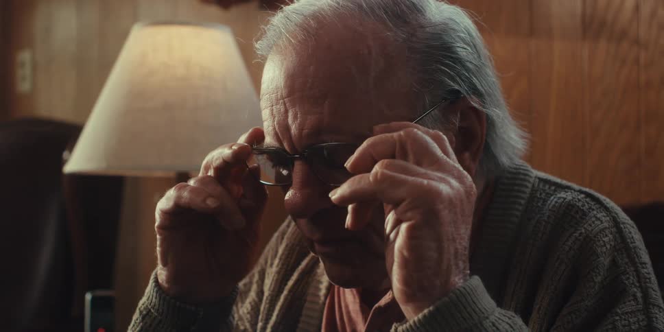 Elderly man sitting at home puts on his eyeglasses before talking