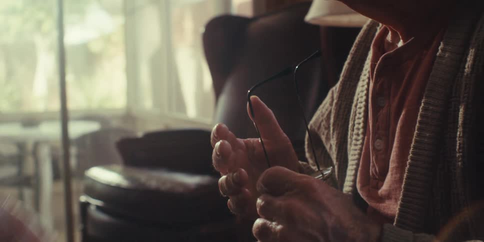 A nurse wearing gloves holds the hands of an elderly man to console him in a home setting