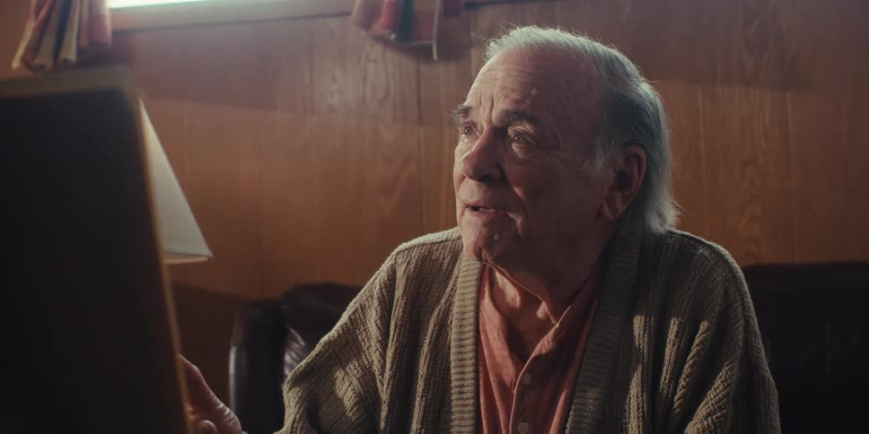 An elderly man laughs as he talks to another person