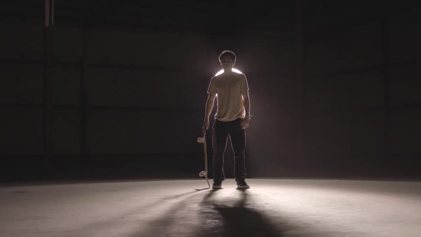 A teenager is standing and holding a skateboard