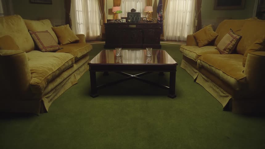 Two yellow sofas face each other across a wooden coffee table in a living room with a large wooden cabinet adorned with lamps and decorations against the back wall all set on a green carpet