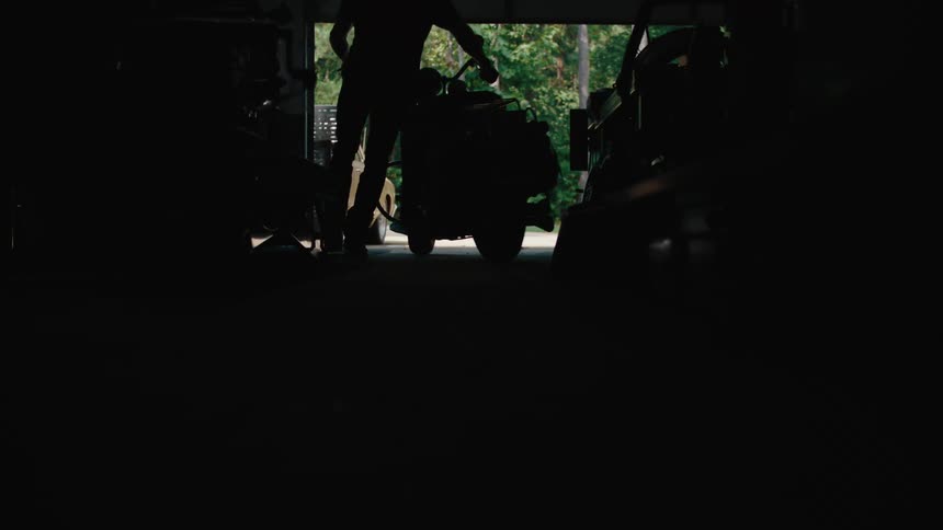 A man is taking his motorcycle out of the garage