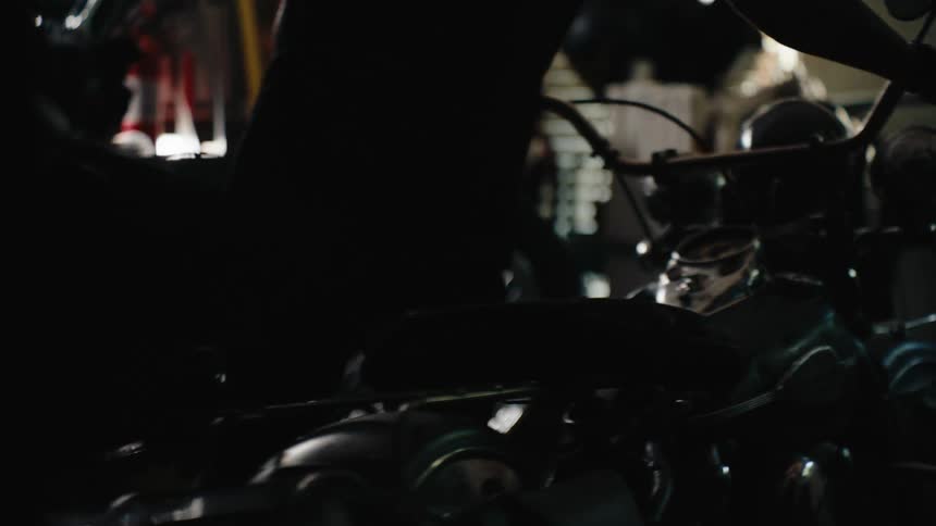 Silhouette of a person walking and carrying a motorcycle inside a garage