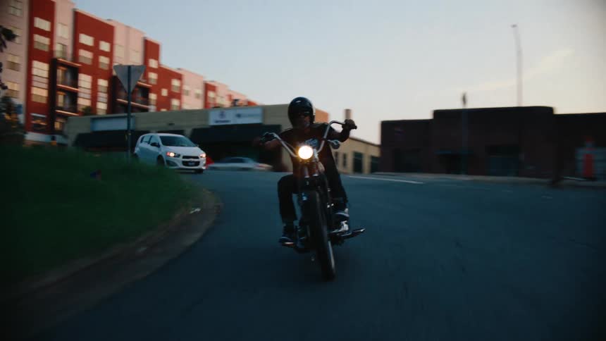A motorcyclist rides along a curved urban road in the city at sunset
