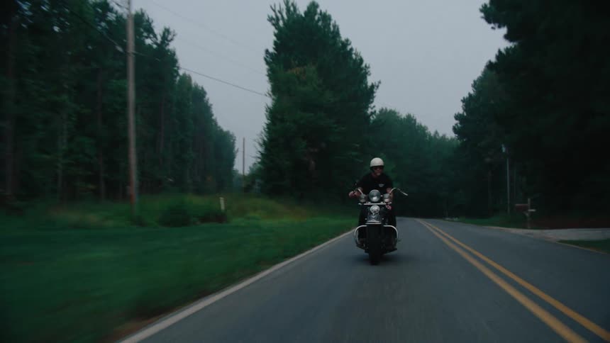 A motorcyclist navigates a curving road bordered by lush dense forest