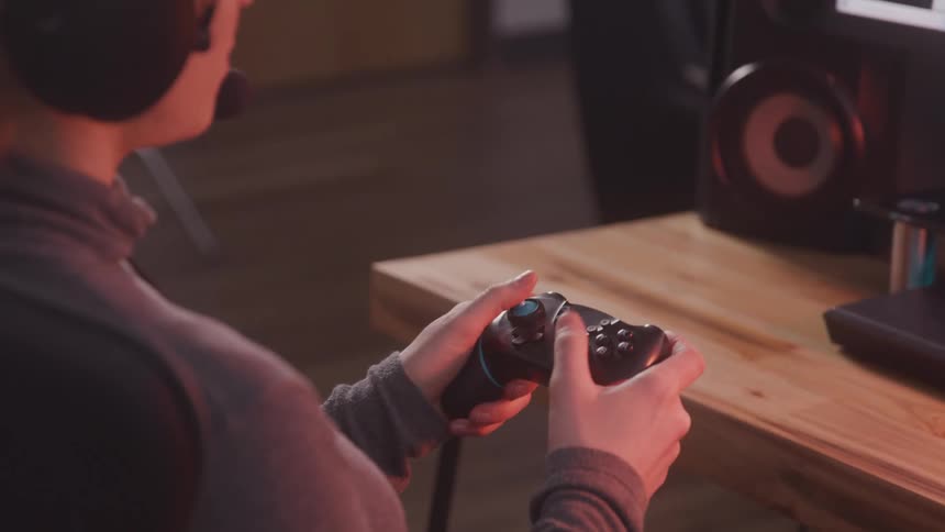 A closeup of a persons hand holding a video game controller while playing at home