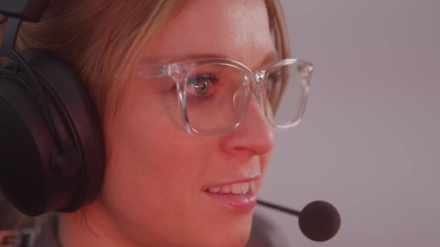 A closeup of a woman wearing glasses and headphones with a microphone focused on a screen in a call center