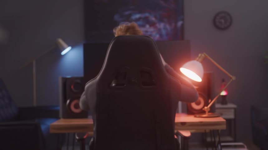 A woman enters a room sits in a gaming chair puts on headphones and begins playing video games