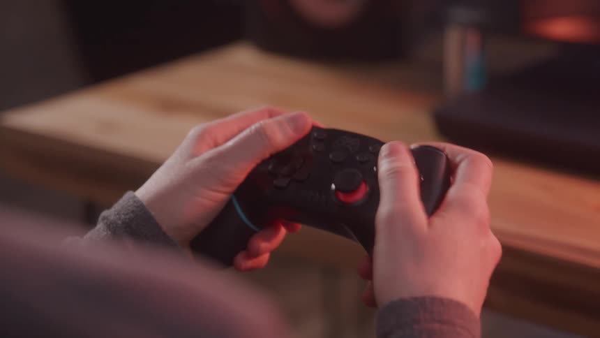 A closeup of a persons hand holding a video game controller while playing at home
