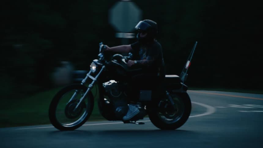A person wearing a helmet rides a motorcycle on a dark road