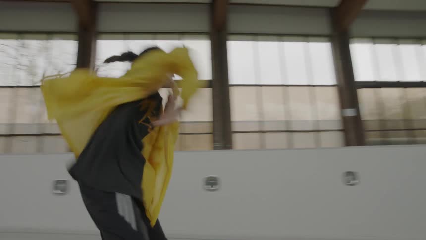 A woman wearing a yellow jacket dances indoors