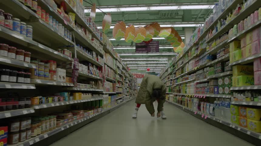 Woman bending over and letting her upper torso hang limply in the middle of a grocery aisle