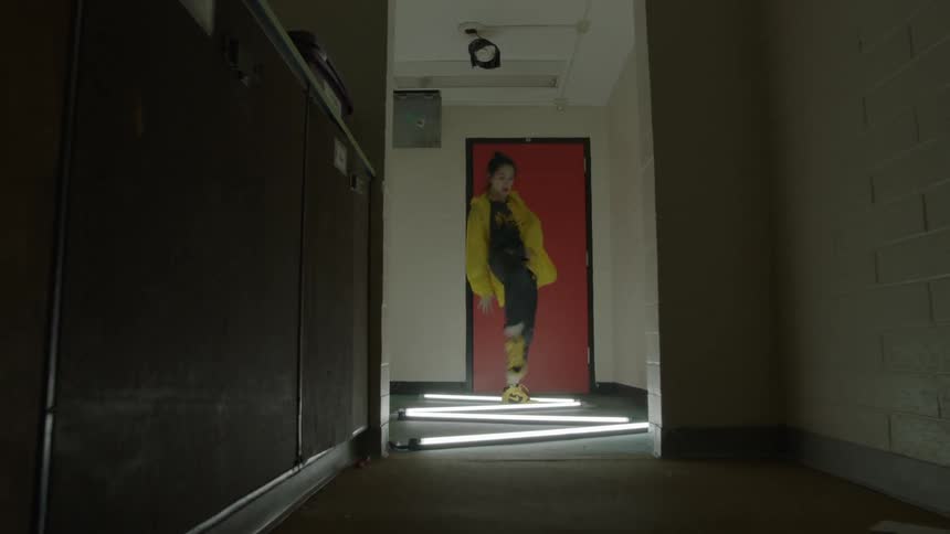 A woman dances in a hallway lit by fluorescent tubes on the floor