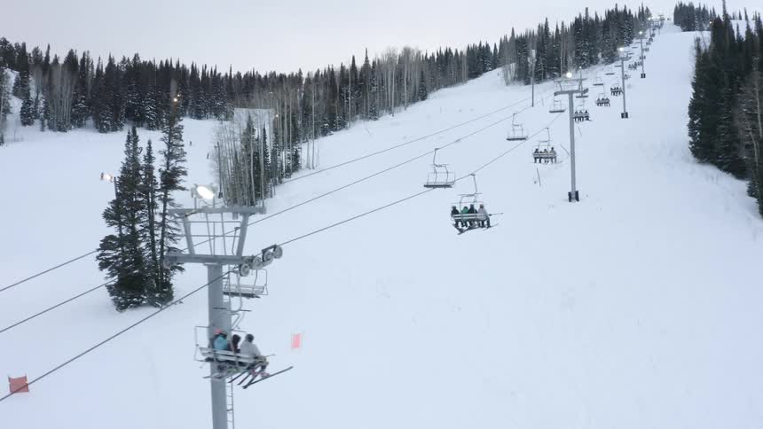 People in chairlifts ascending a snowcovered mountain with trees in the background