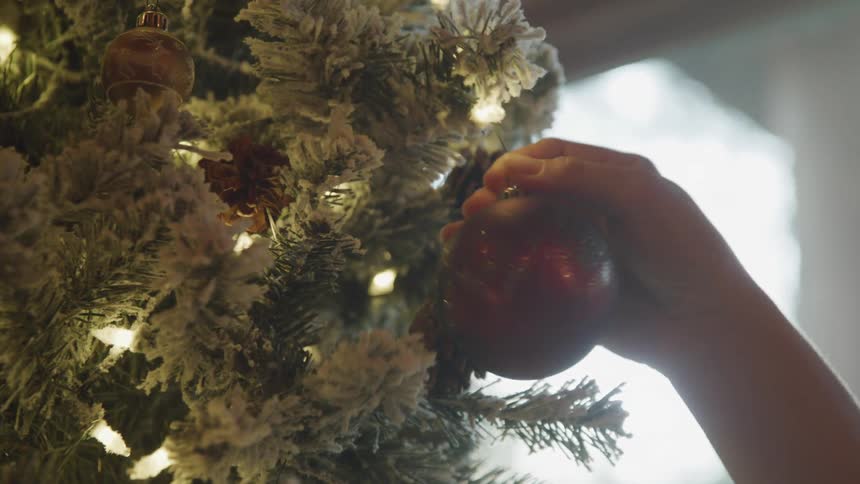 Womans hand placing a christmas ball on an artificial tree decoration