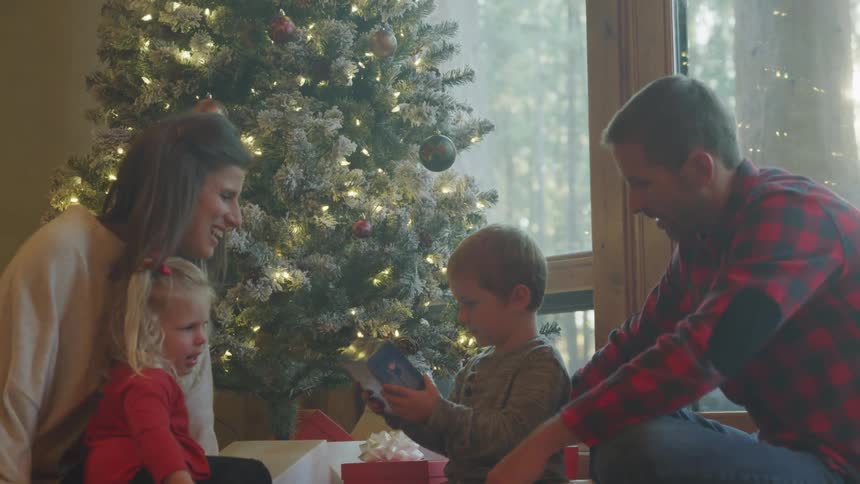Family sitting next to a christmas tree with children looking at presents