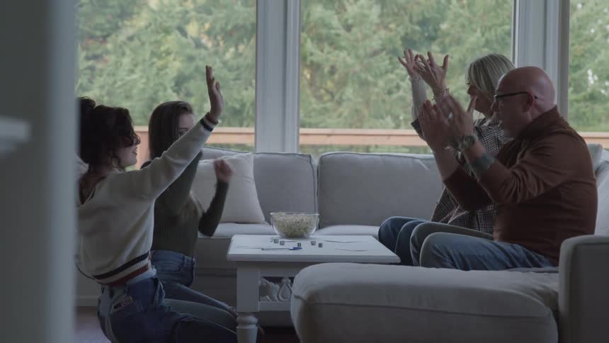 Family playing board game on table and clapping hands happily in living room