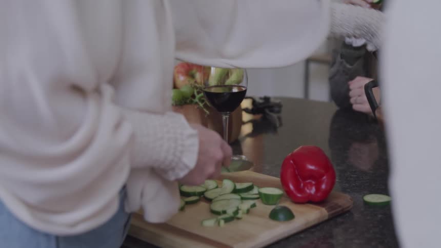 Pair of hands with a knife cutting cucumber on a wooden cutting board in the sink