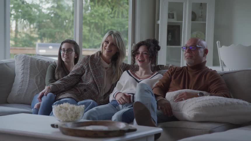 Cheerful family sitting in the living room with popcorn in front of them watching something