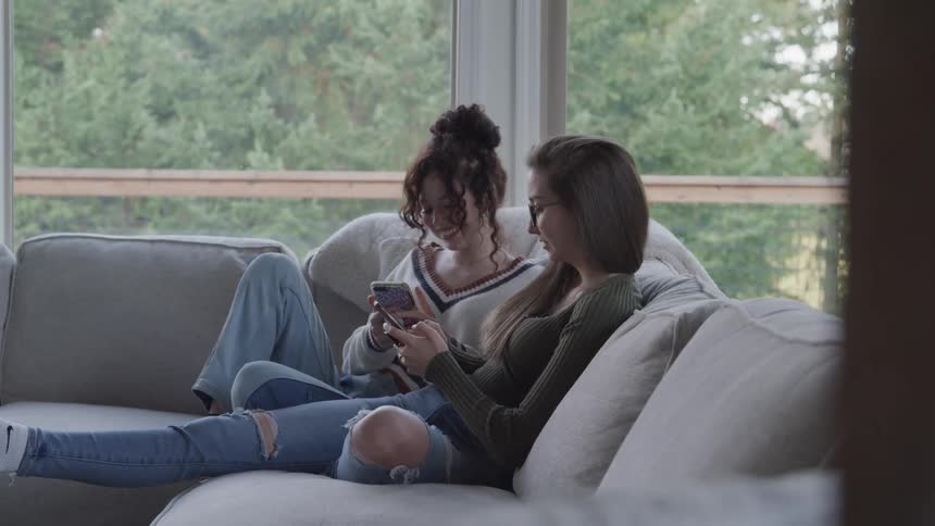 Two teenage girls sitting in the living room using their smartphones