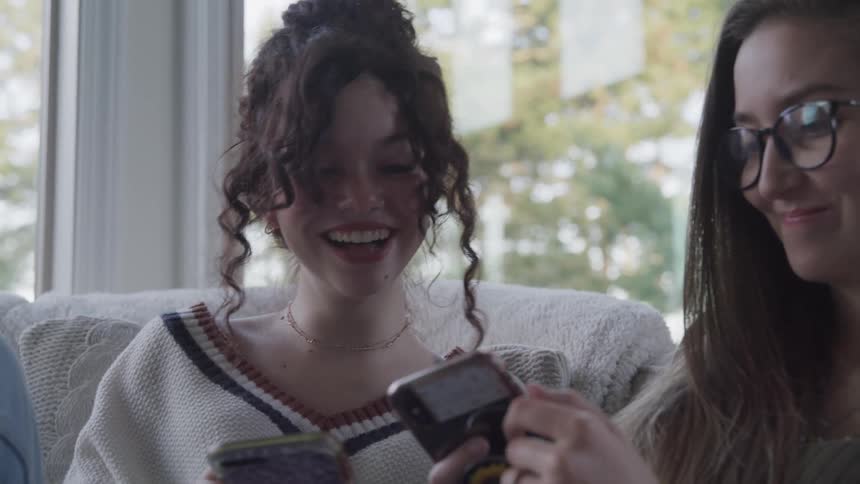Two smiling teenage girls sitting interacting with smartphone