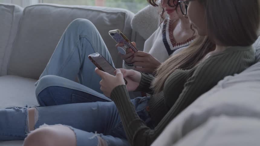 Two teens seated on a couch engrossed in their smartphones