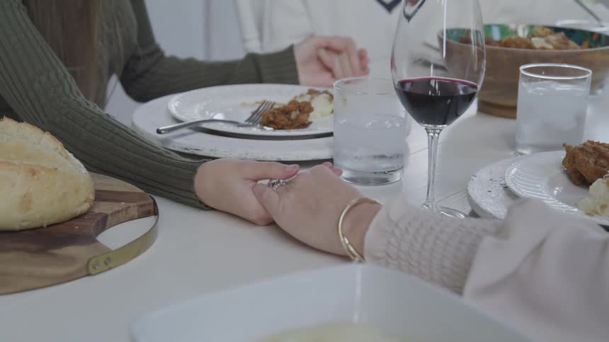People are holding hands as they pray before a meal