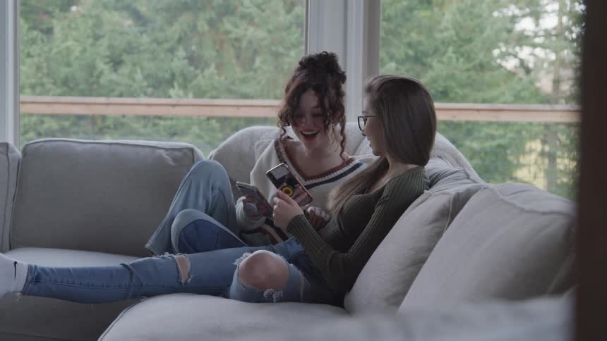 Two young women sitting on a couch interacting with a smartphone