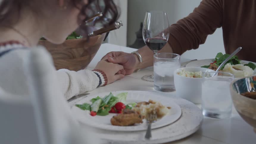 People holding hands at a table served with lunch in a gesture of prayer