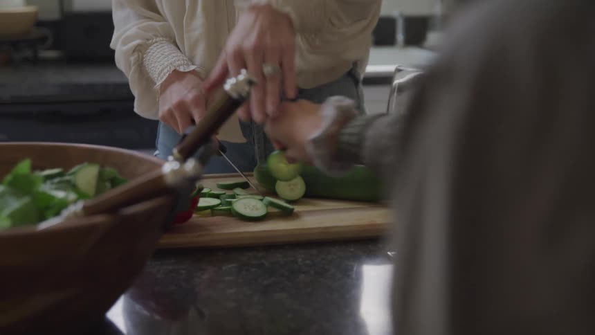 Pair of hands cutting a cucumber and another person taking a slice