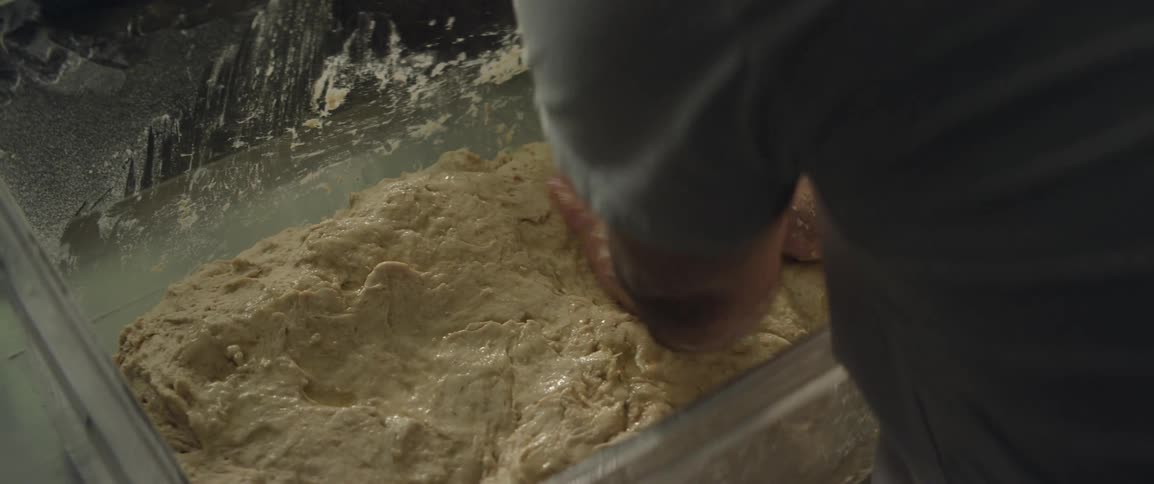 Hands kneading bread dough in a large container