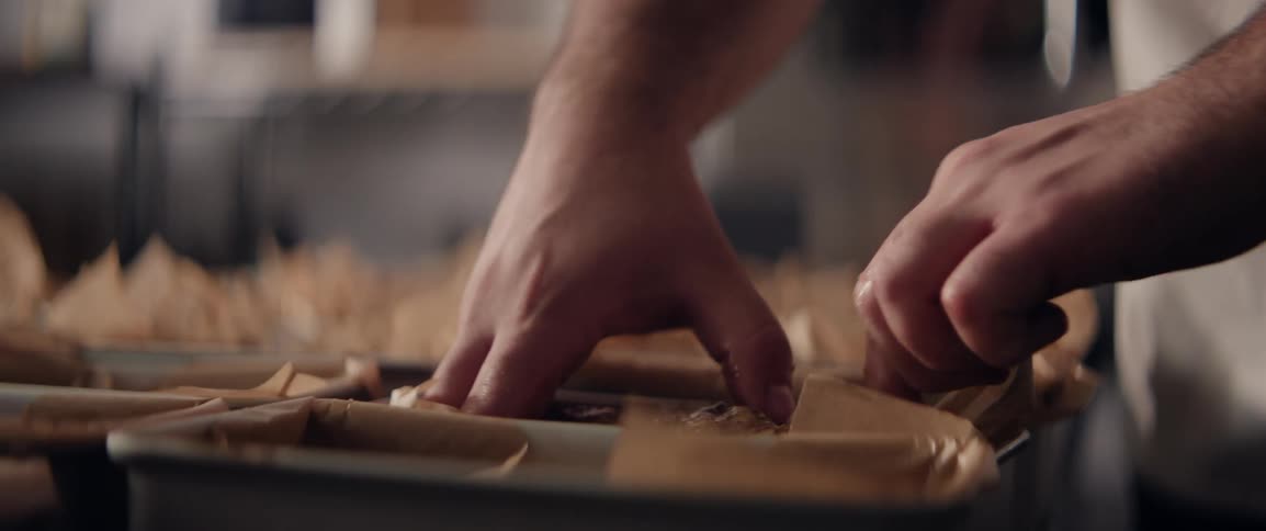 Two hands place dough into metal sheet containers lined with parchment paper on a countertop