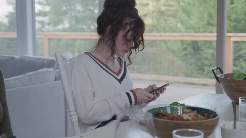 Teenage girl sitting at a table served with lunch typing on a smartphone