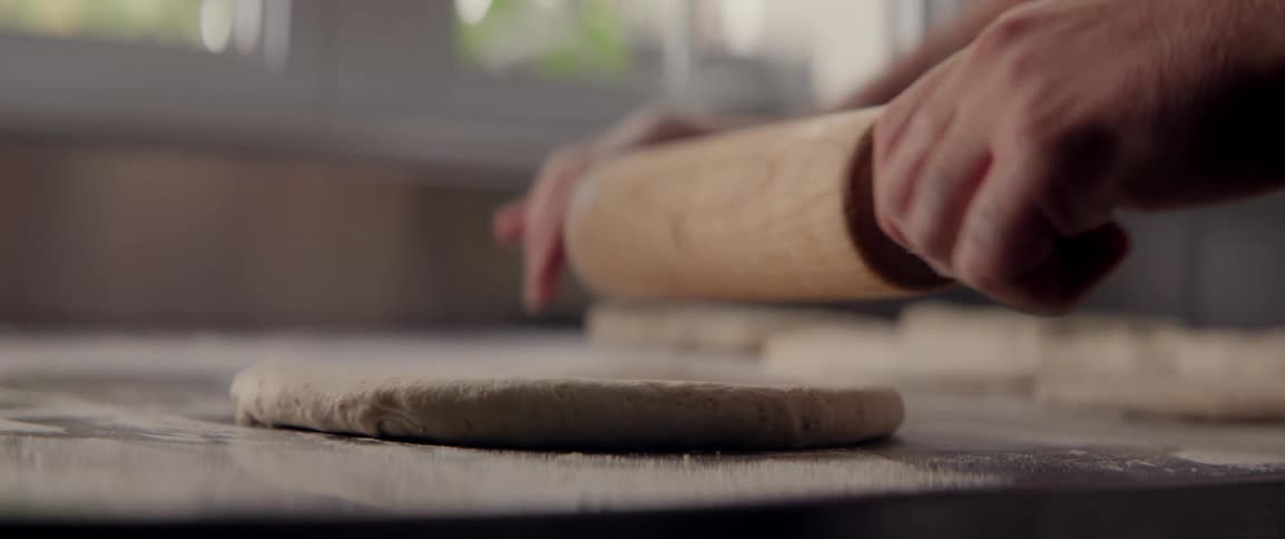 A person rolls out dough on a floured surface using a wooden rolling pin