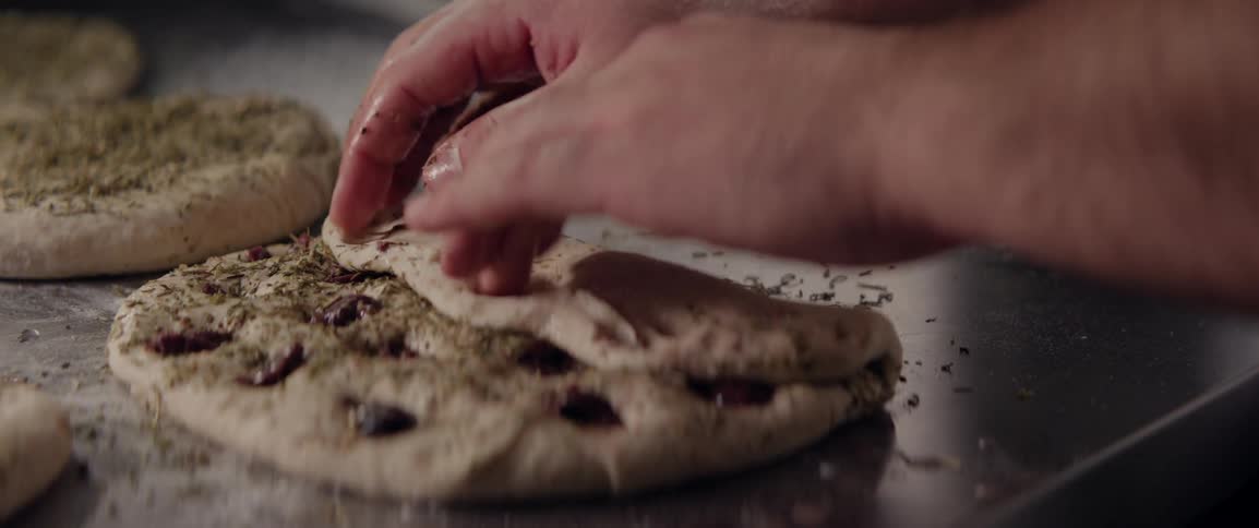 A baker is folding dough over on a metal counter
