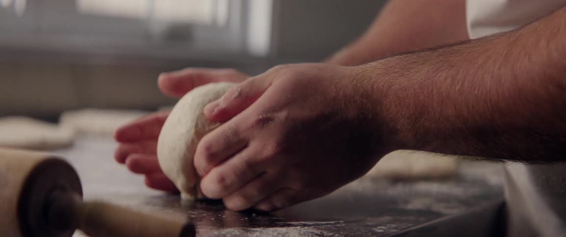 Pair of hands making an oval shape of bread out of raw dough