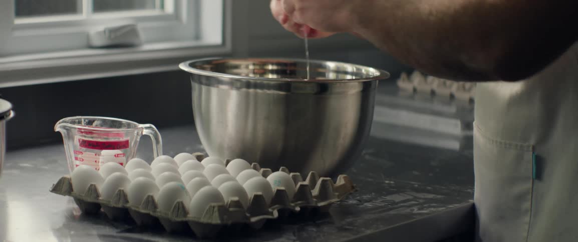 Pair of hands breaking eggs and pouring them into a metal container