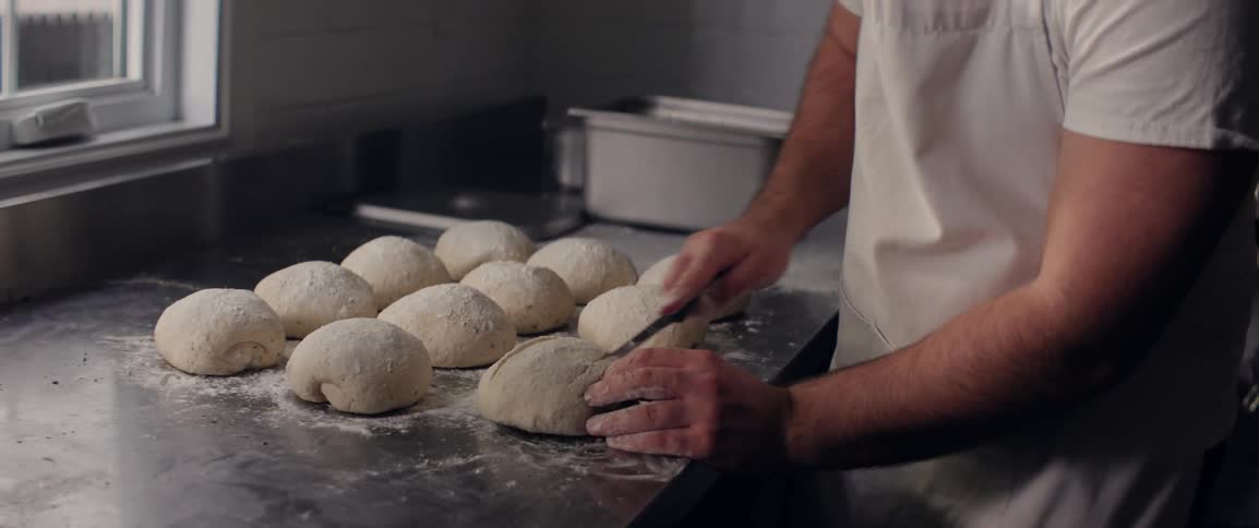 A person with a knife making cuts in raw bread dough