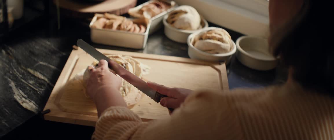 A person slices bread with a knife in a kitchen
