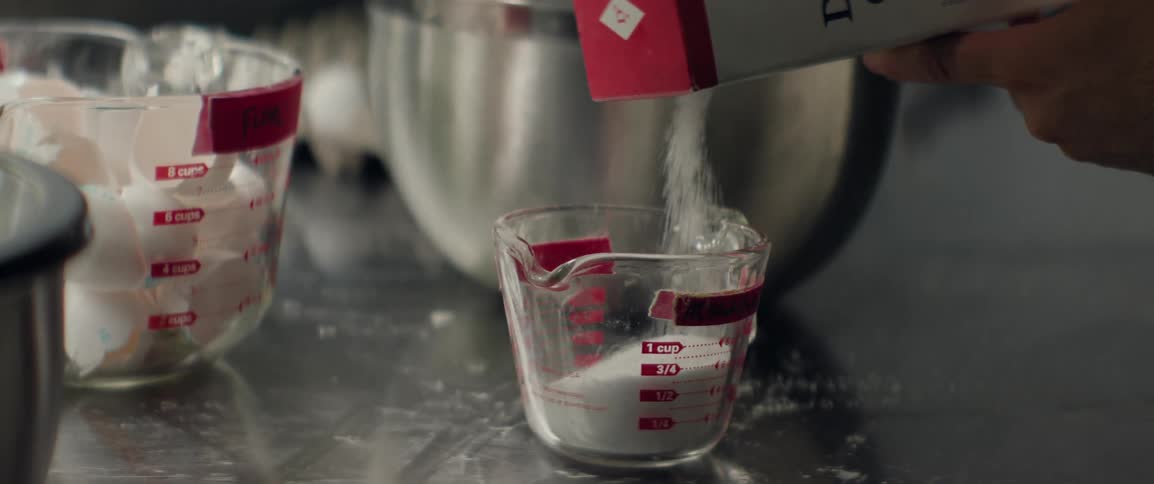 Sugar being poured into a glass measuring cup in an industrial kitchen