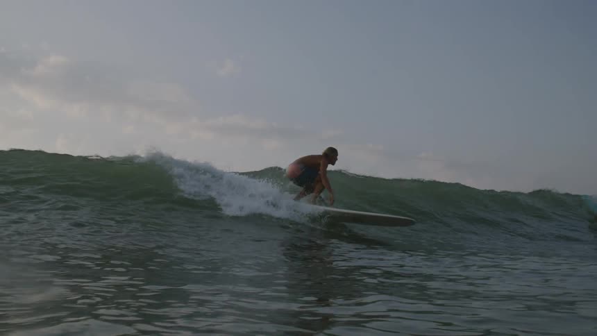 A lone surfer is riding a wave in the ocean under a cloudy sky